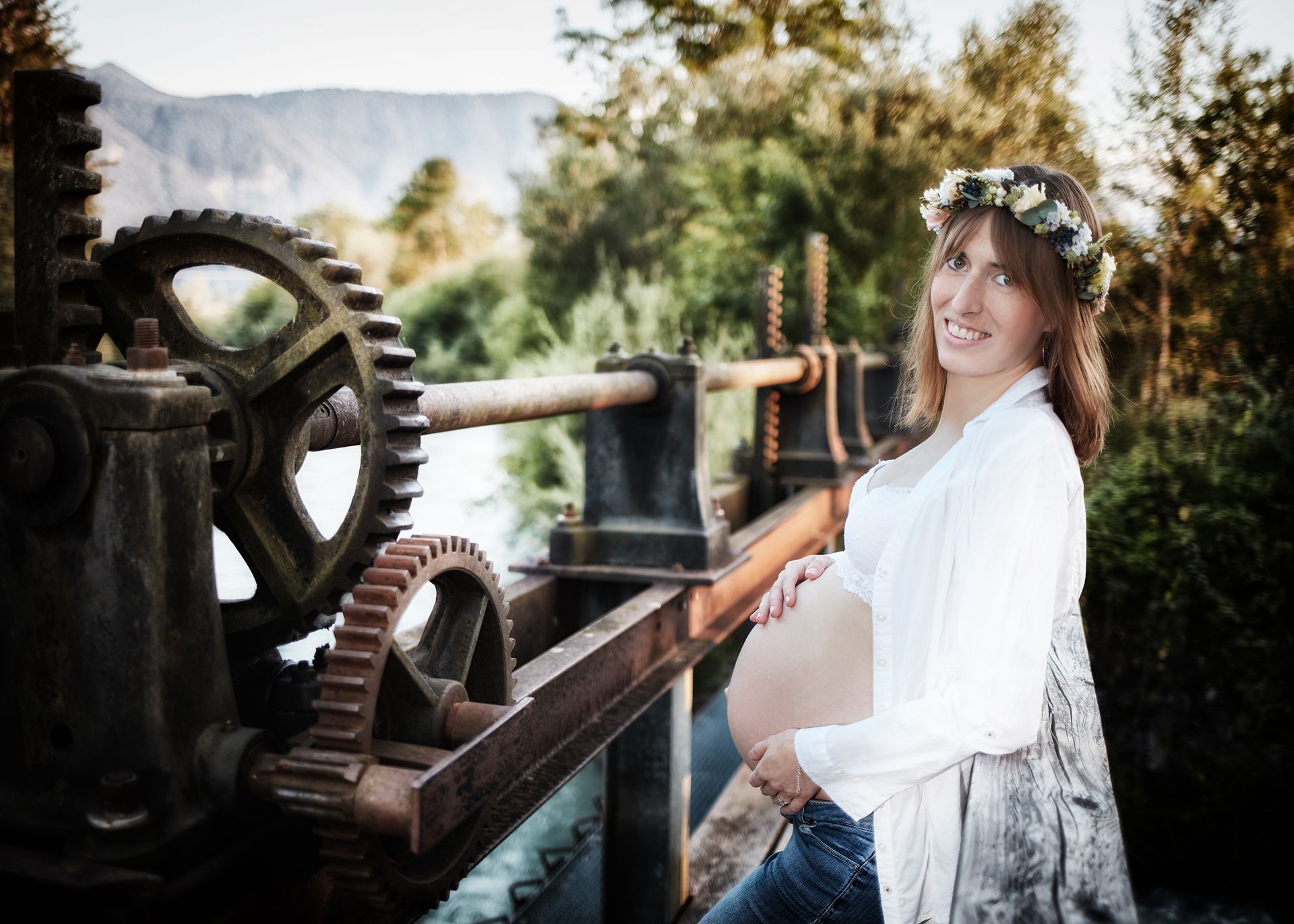 Schwangere Frau im Freien lehnt an einem alten Metallrad und trägt einen Blumenkranz.