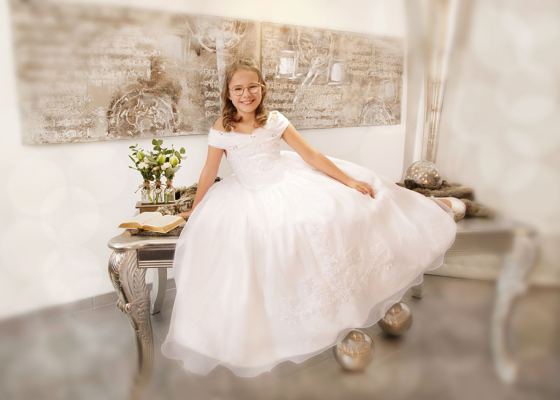 Mädchen in einem weißen Kleid sitzt elegant auf einem dekorativen Möbelstück.