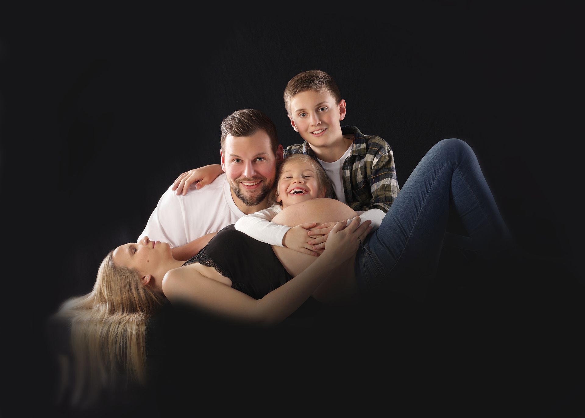 Familienporträt von Eltern mit Kleinkind, liegend und lachend im Studio.