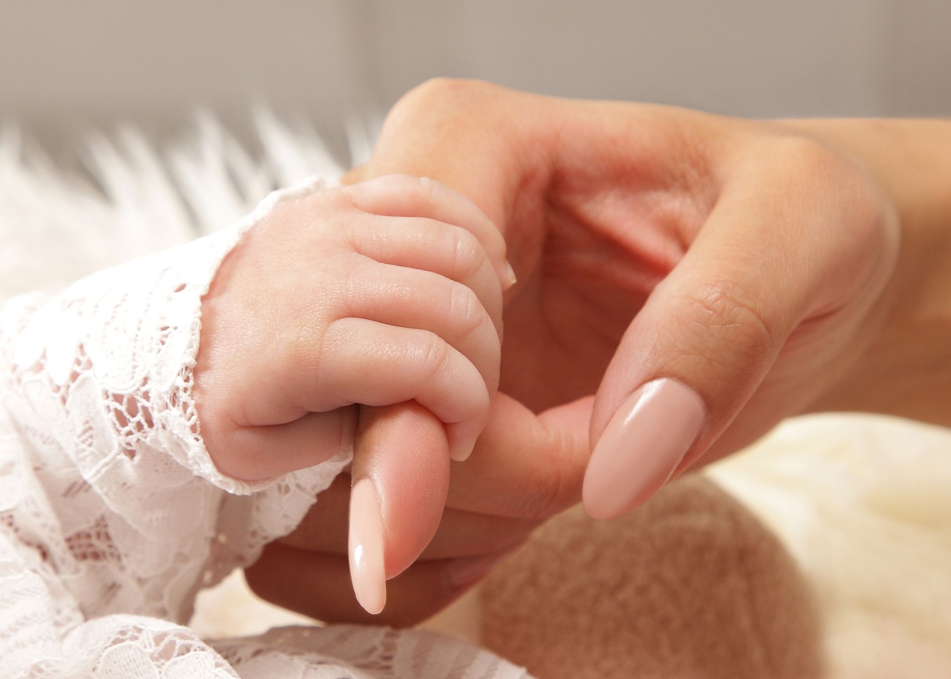 Nahaufnahme einer Erwachsenenhand, die sanft die Hand eines Babys hält.