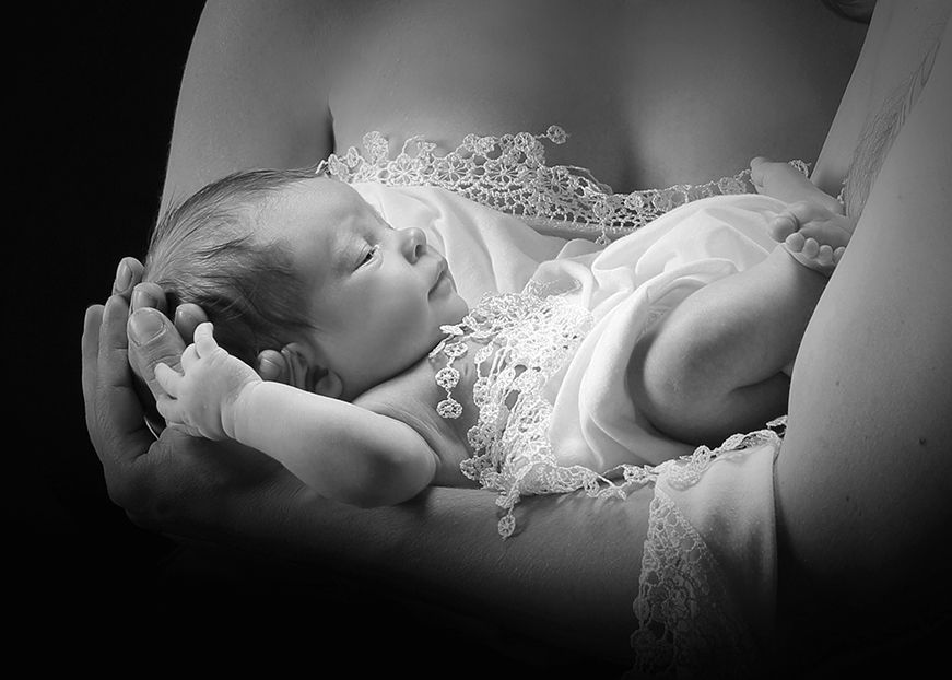 Schwarz-weiß-Foto eines Neugeborenen, das in den Armen eines Erwachsenen schläft.