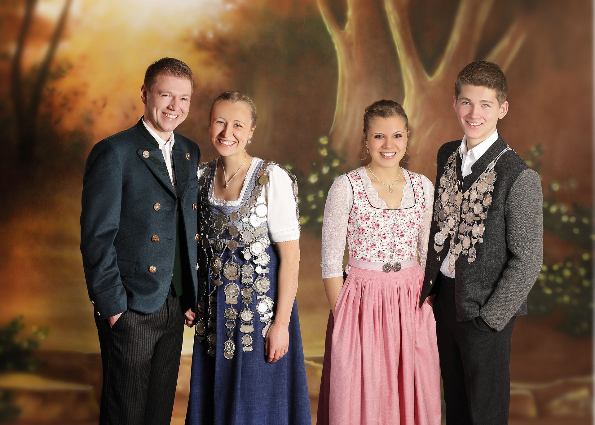 Vier Personen in festlicher Tracht stehen lächelnd vor einem warmen Hintergrund.