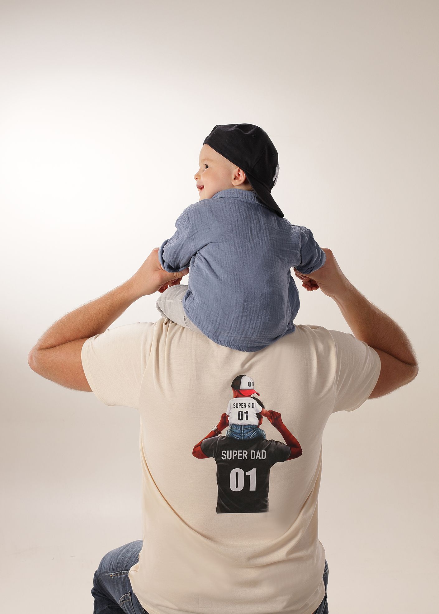 Junge mit Mütze sitzt seitlich und lehnt sich an einen Erwachsenen.