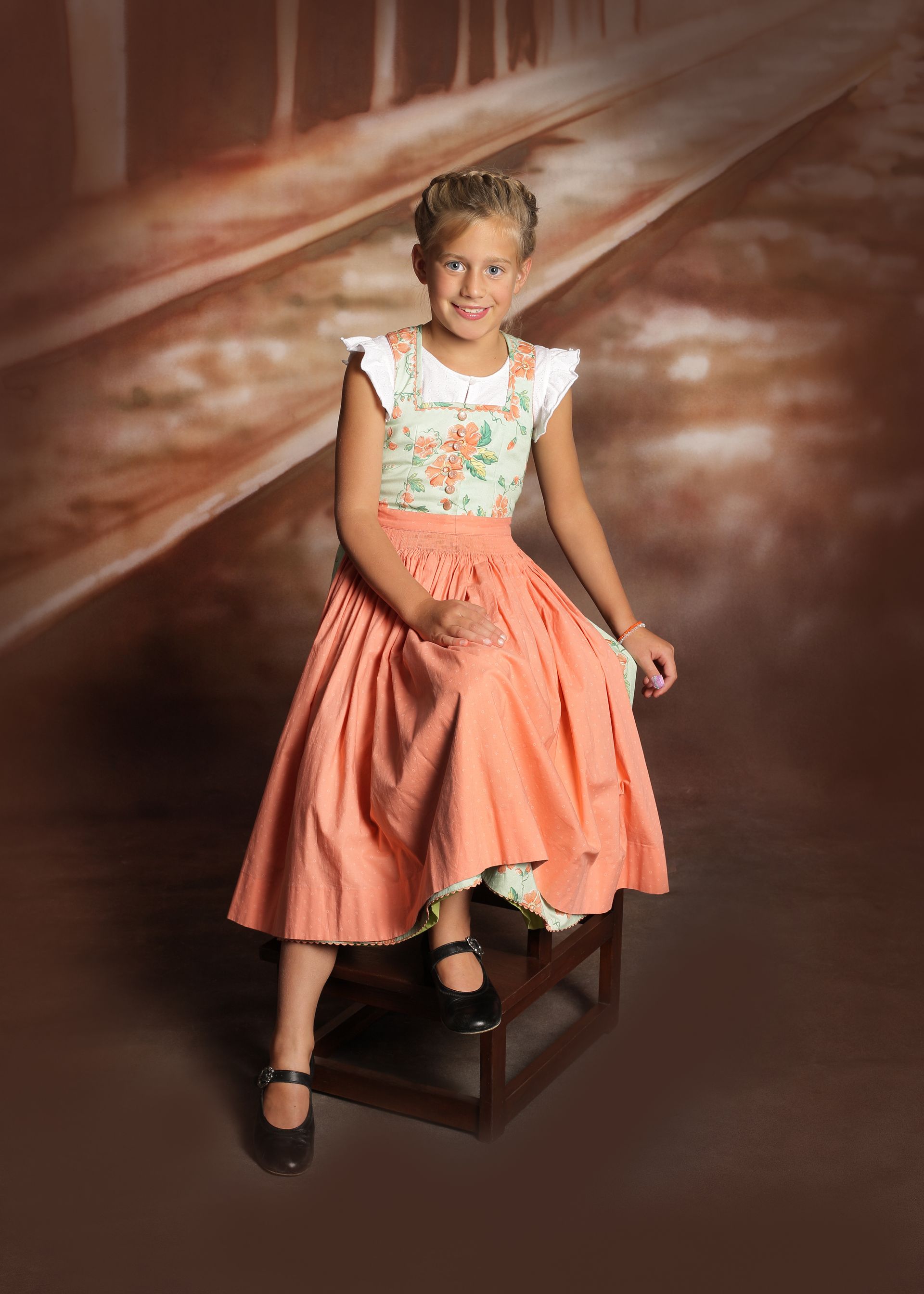 Mädchen in einem Sommerkleid lächelt vor einem warmen Studiobackdrop.