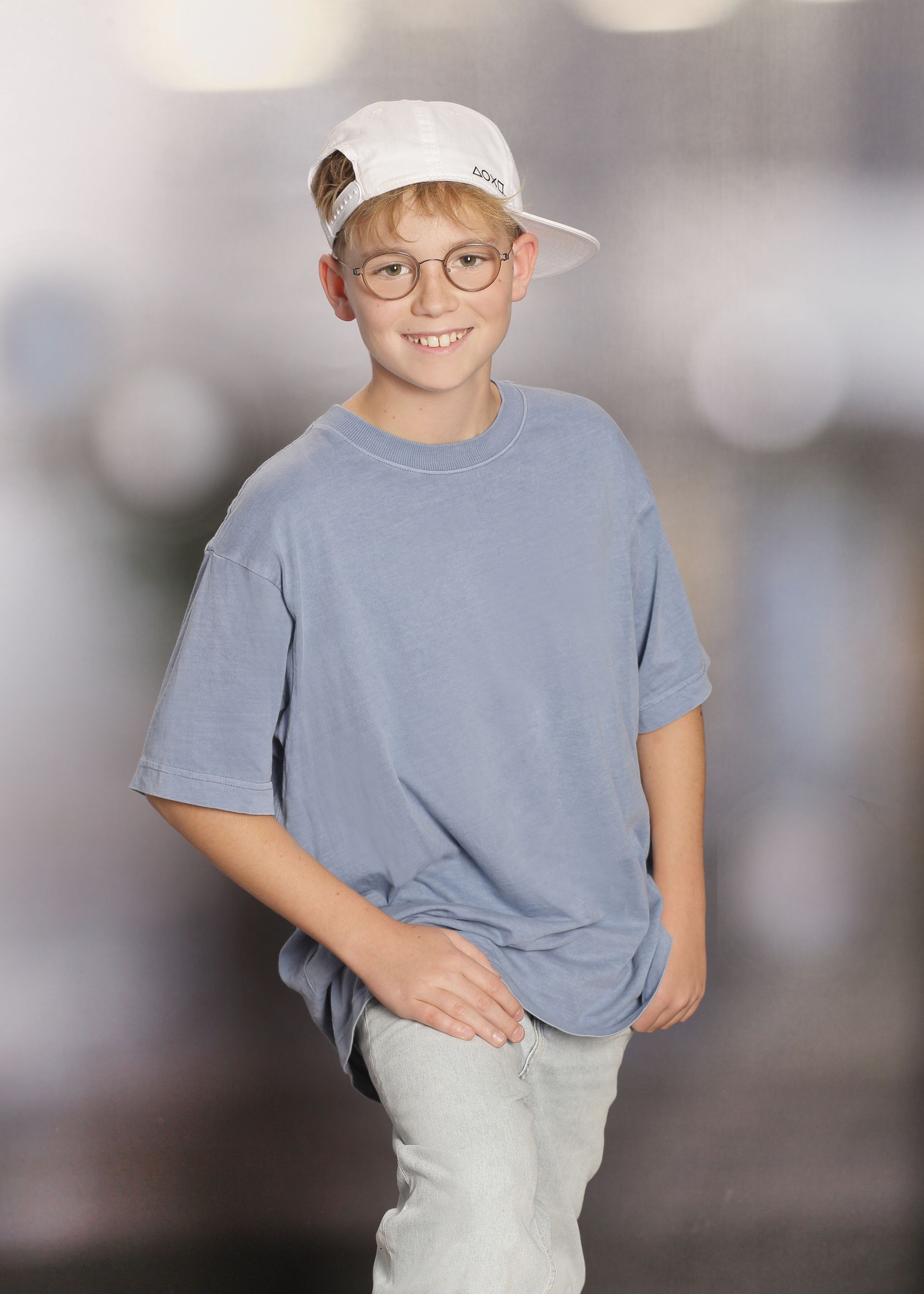 Junge mit Brille und Basecap lächelt vor einem unscharfen, hellen Hintergrund.