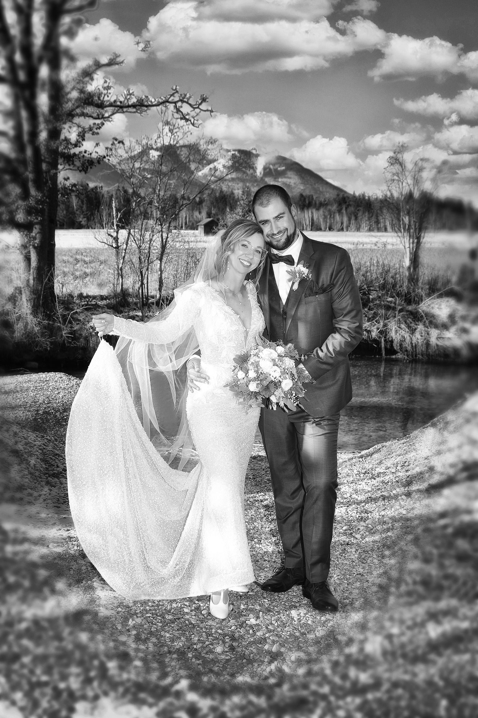 Schwarz-weiß-Aufnahme eines Paares mit Bergen und See im Hintergrund.