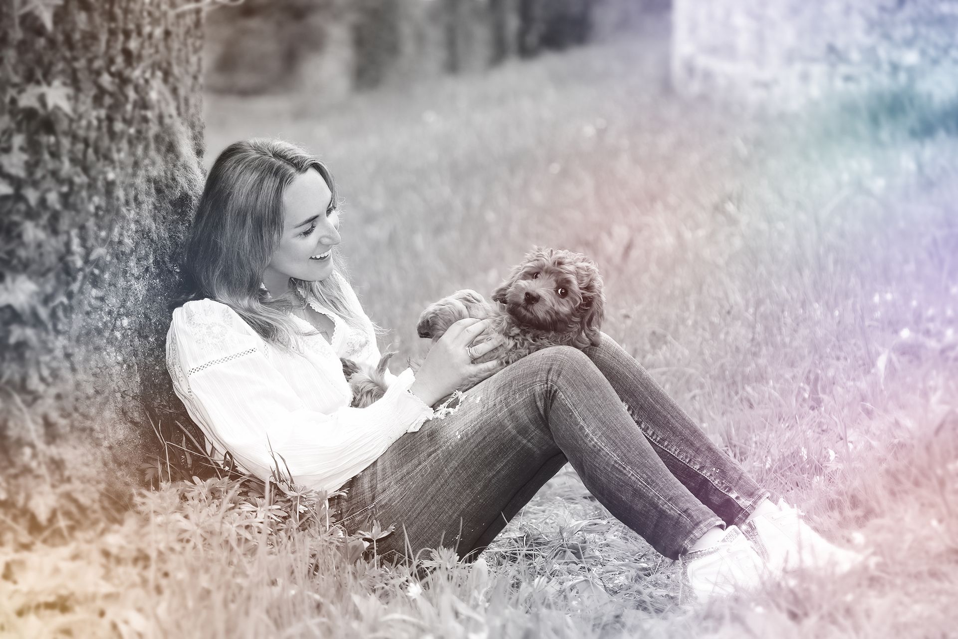 Schwarz-weiß-Aufnahme einer Frau, die im Gras sitzt und mit einem Hund spielt.