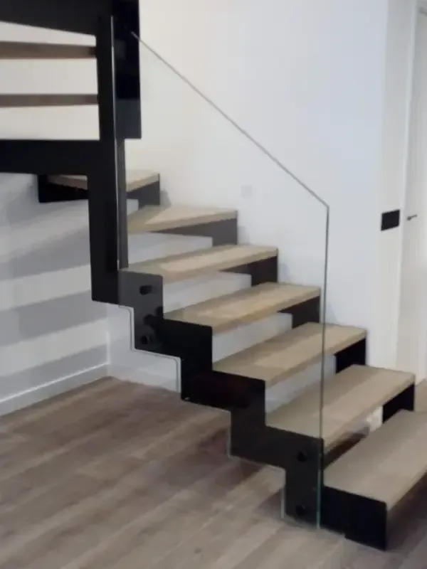 Una moderna escalera con peldaños de madera clara y barandilla de cristal transparente.