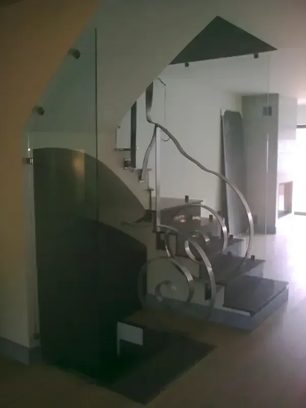 Escalera moderna con peldaños flotantes, barandillas de cristal y un pasamanos decorativo de metal curvado