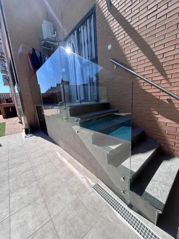 Una barandilla de cristal instalada en el lateral de una escalera de piedra gris que conduce a un edificio de ladrillo.