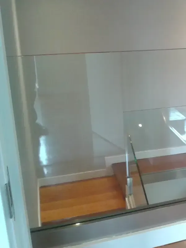 Una barandilla de cristal separa una escalera con peldaños de madera y una elegante base metálica