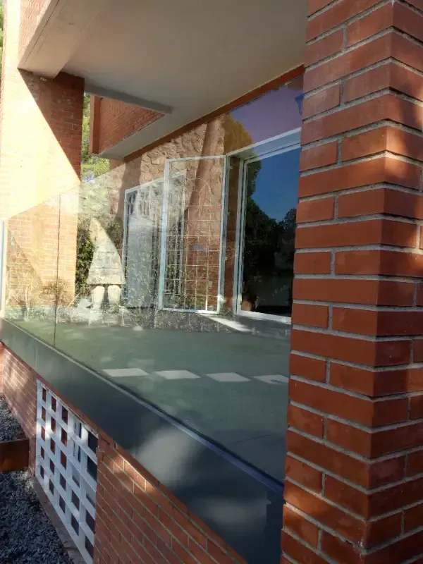 Un patio de ladrillo con barandilla de cristal, cerca de una puerta de cristal