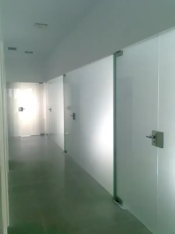 Un pasillo revestido con elegantes puertas de cristal blancas que van desde el suelo hasta el techo, con tiradores plateados