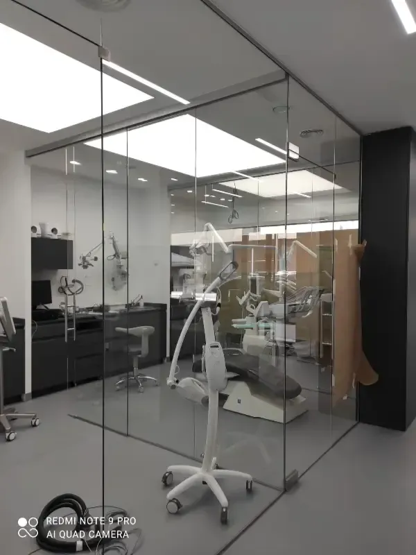 Una moderna sala de exploración dental con paredes de cristal, equipada con sillón dental e instrumental médico.