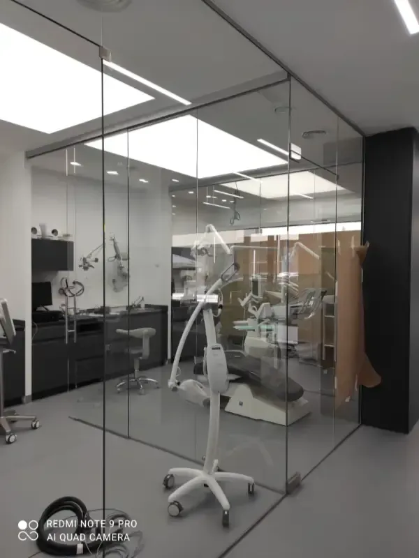 Consultorio dental moderno, con paredes de cristal, sillón dental, instrumental y una iluminación tenue en el techo.