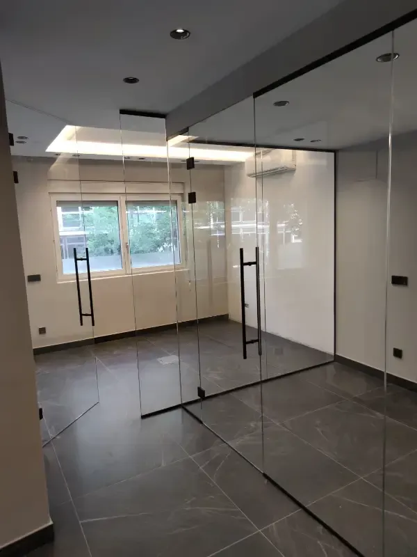 Un espacio de oficina moderno y minimalista con paredes blancas y paredes de cristal con tiradores negros.