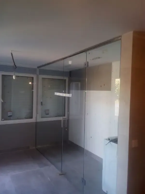 Mamparas de cristal con estructura metálica instaladas en una habitación con paredes blancas y suelo gris.