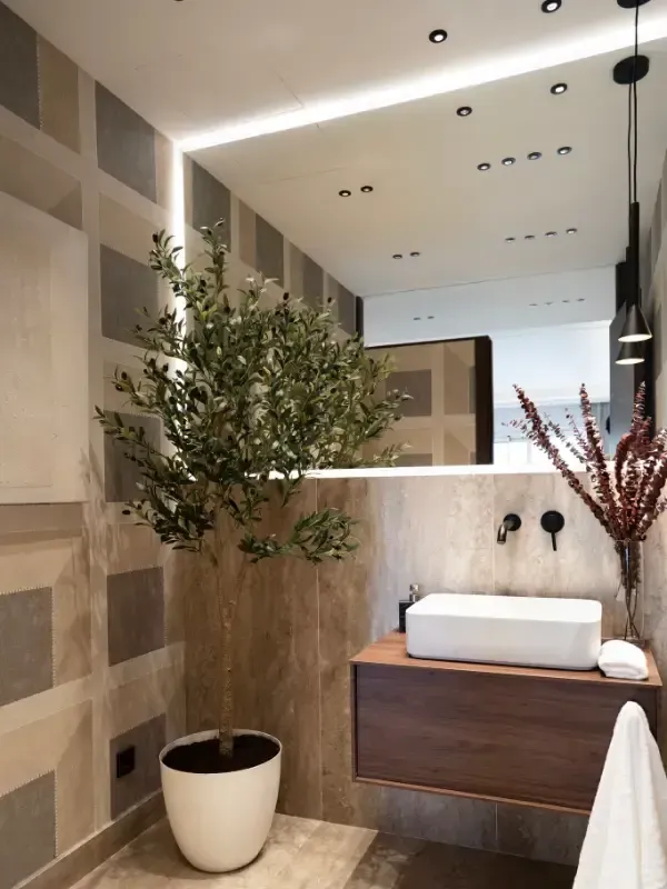Un baño moderno con lavabo blanco sobre encimera de madera, azulejos decorativos en la pared y un espejo grande.