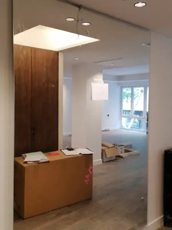 Un gran espejo que abarca toda la pared refleja una habitación en construcción, con cajas de cartón en el suelo