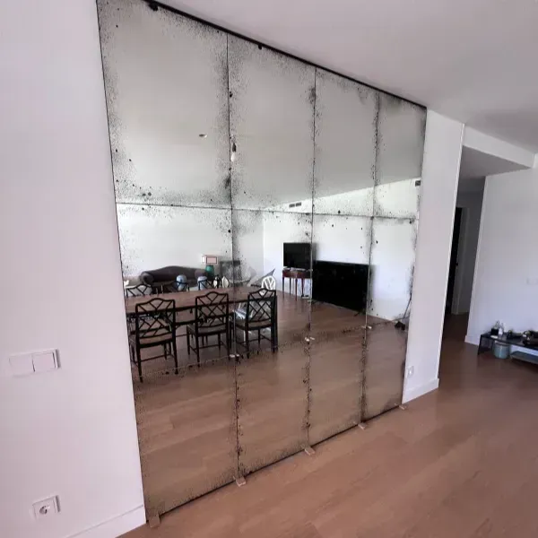 Una pared de espejos de estilo antiguo que va del suelo al techo refleja un comedor con una mesa de madera