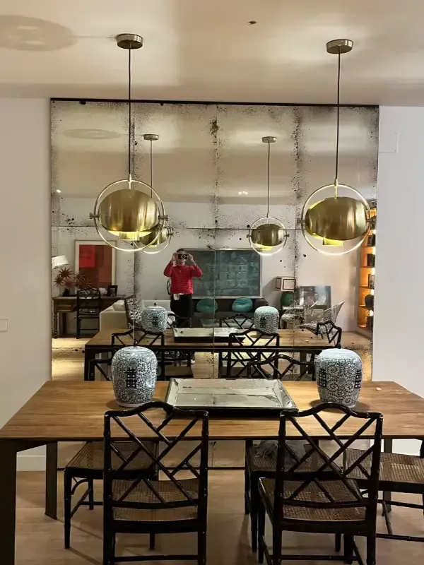 Un comedor con una mesa de madera, sillas negras estampadas y un gran espejo de pared.