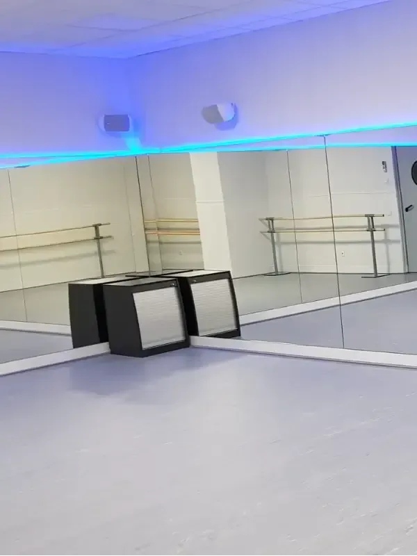 Un estudio de danza con espejos de pared a pared, barras de ballet, un altavoz portátil negro en el suelo