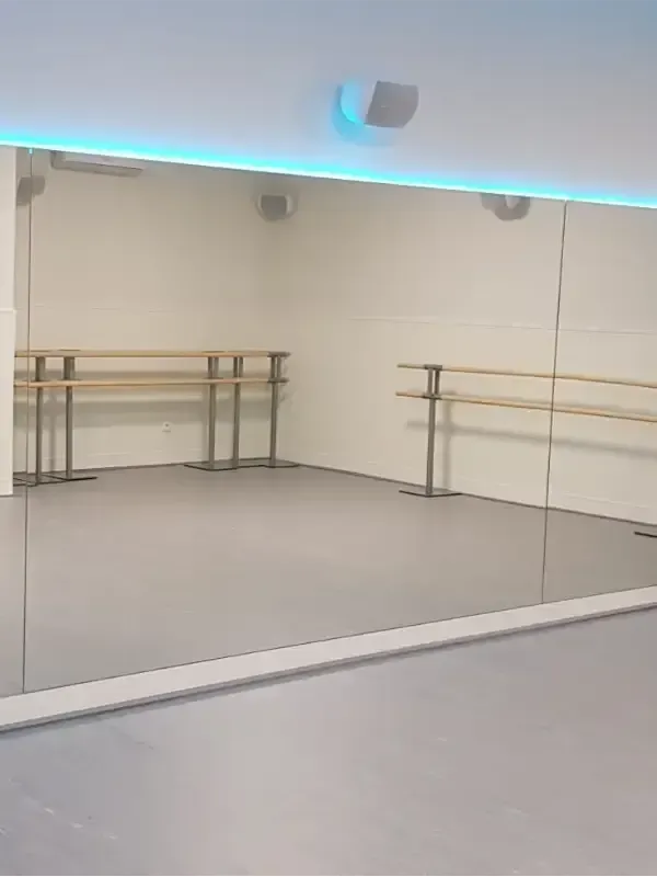 El interior de un estudio de danza con un gran espejo en la pared, barras de ballet e iluminación ambiental azul.