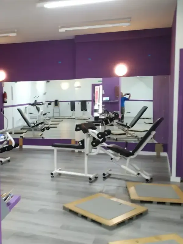 El interior de un gimnasio con máquinas de ejercicio sobre un suelo gris, reflejado en un gran espejo.