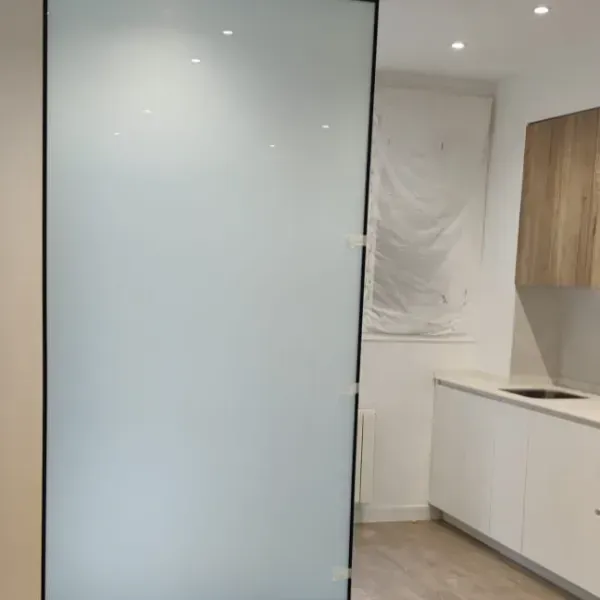 Un separador de ambientes con un panel de vidrio mate esmerilado en un marco negro, situado en una cocina