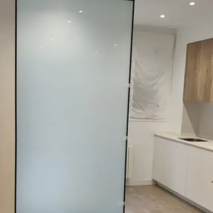 Un separador de ambientes con un panel de vidrio mate esmerilado en un marco negro, situado en una cocina
