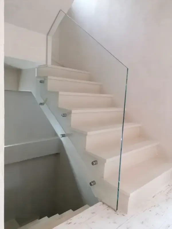 Escalera moderna de color blanco roto con barandilla de cristal sin marco montada en el lateral con separadores de acero