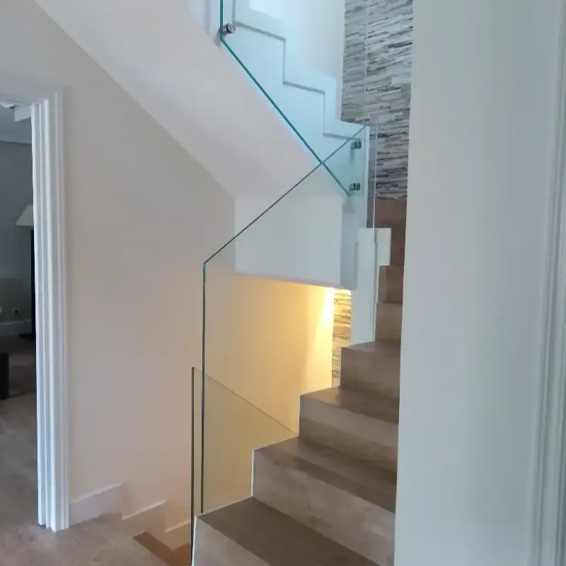 Escalera moderna con peldaños de madera clara, barandilla de cristal y pared decorativa revestida de azulejos de piedra