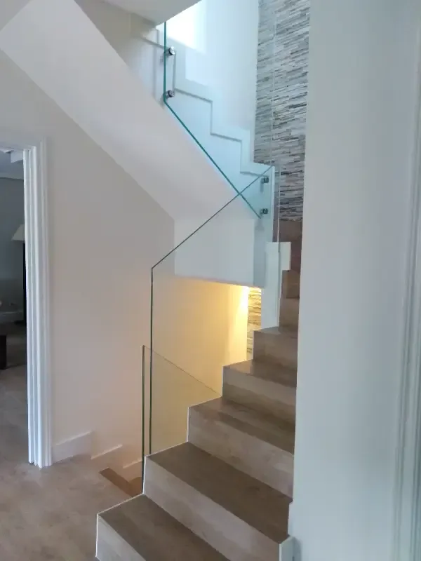Escalera moderna de madera con barandilla de cristal y pared decorativa de piedra texturizada en un interior residencial.