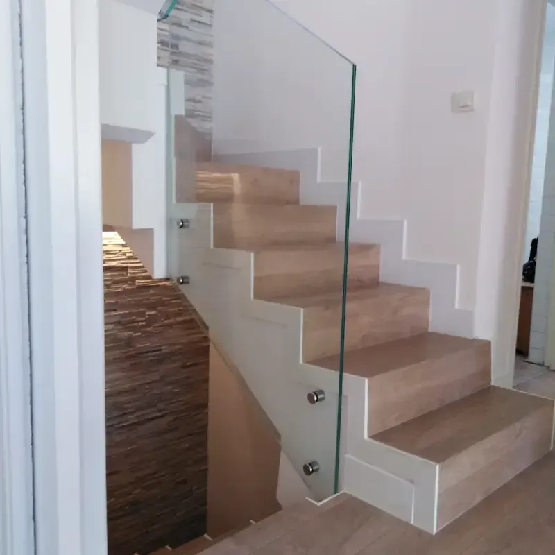 Una escalera moderna con escalones de madera clara y una barandilla de cristal transparente sujeta con pernos metálicos.