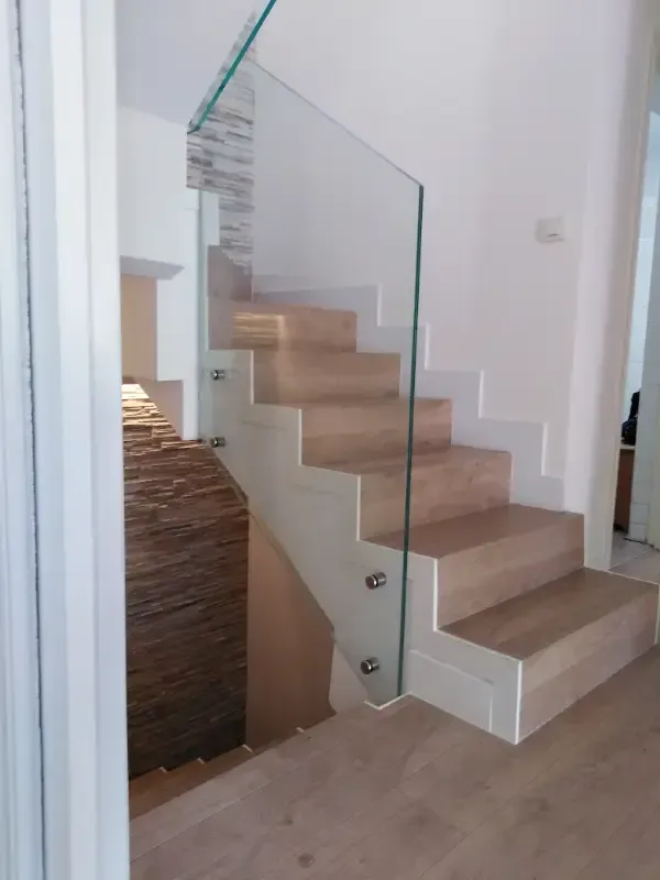 Una escalera moderna con escalones de madera clara, una barandilla de cristal sin marco y paredes decorativas de piedra