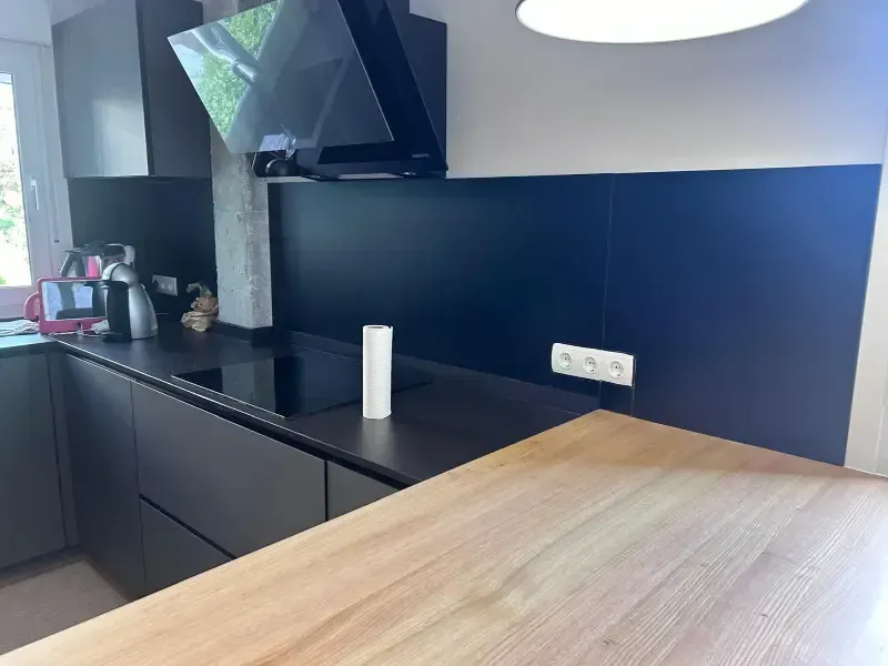 Una cocina moderna con una encimera de madera clara, protector contra salpicaduras negro y campana extractora.