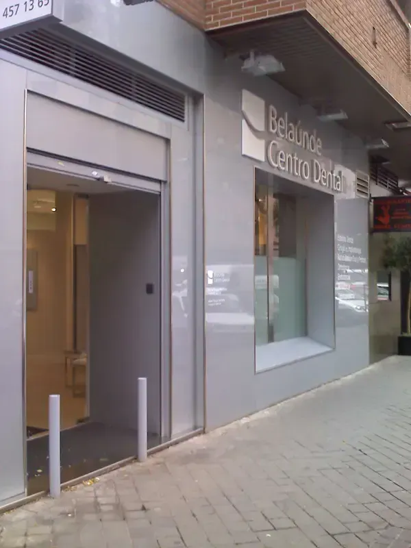 Entrada a una clínica dental, que presenta una fachada gris, una ventana de cristal y una puerta de acceso empotrada.