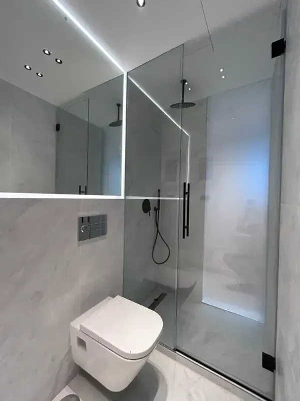 Un baño moderno y minimalista con paredes de mármol gris, un inodoro blanco suspendido y una ducha con mampara de cristal.