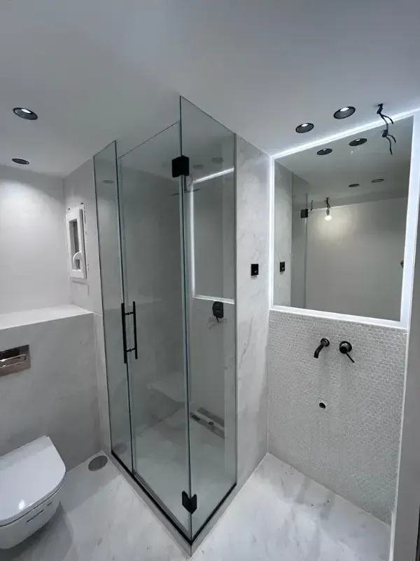 Un moderno baño blanco con ducha a ras de suelo con mampara de cristal, inodoro suspendido y tocador con espejo