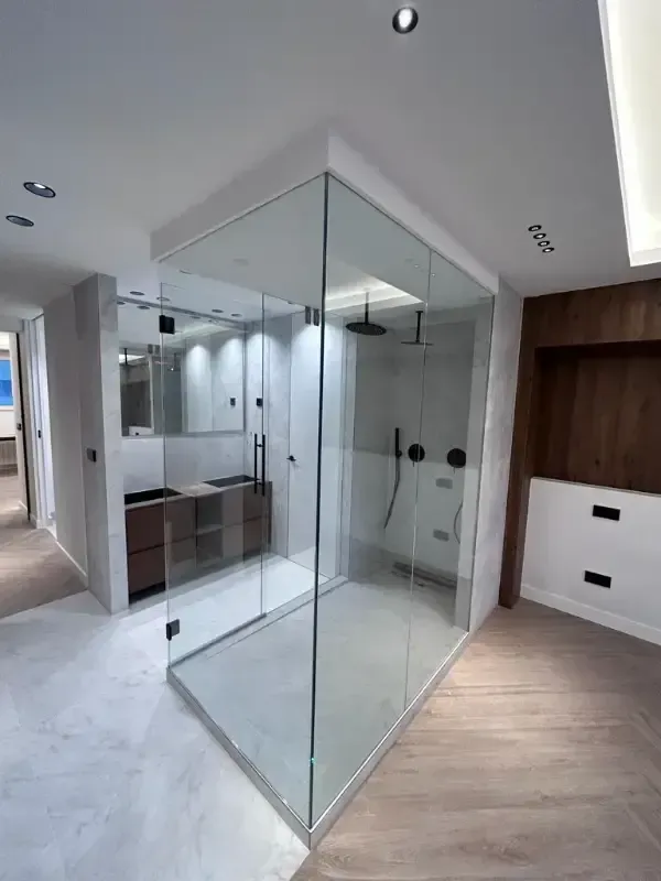 Un baño moderno con ducha acristalada, tocador en tono madera y suelo de baldosas claras.