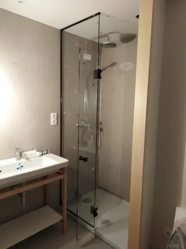 Un baño moderno con un lavabo blanco sobre un mueble de madera clara, junto a una ducha con mampara de cristal