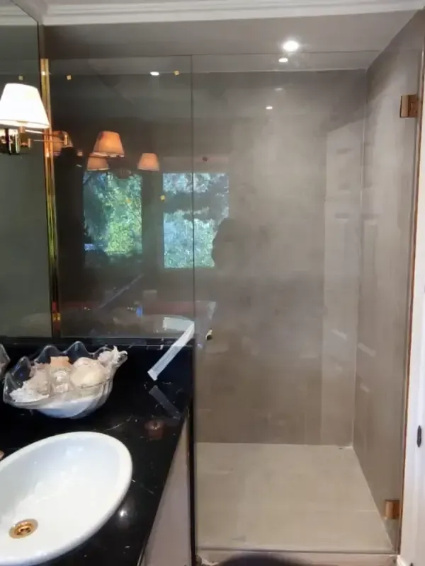 Un baño moderno con ducha acristalada, encimera negra y lavabo blanco junto a un cuenco decorativo.
