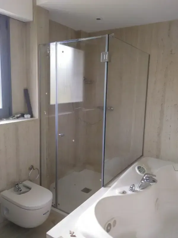 Un baño moderno con ducha acristalada, bañera blanca e inodoro suspendido sobre paredes de tonos neutros.