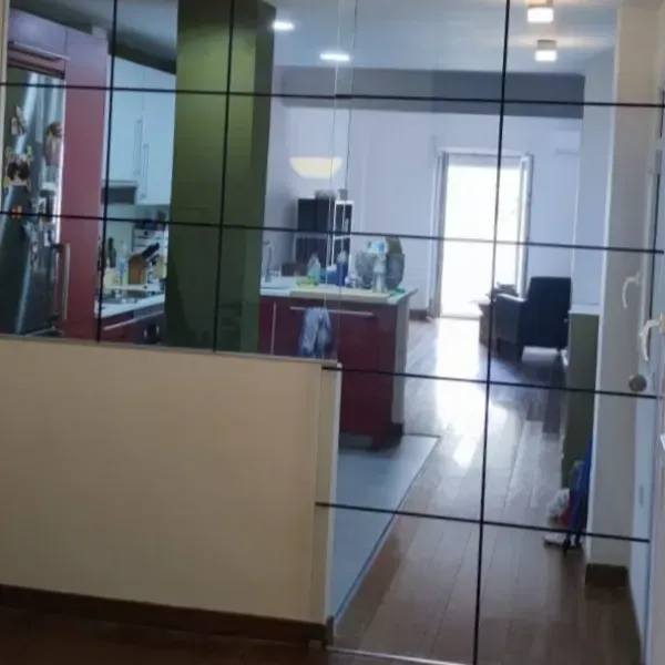 Un separador de ambientes de vidrio con diseño de cuadrícula que obstruye parcialmente la vista hacia una cocina