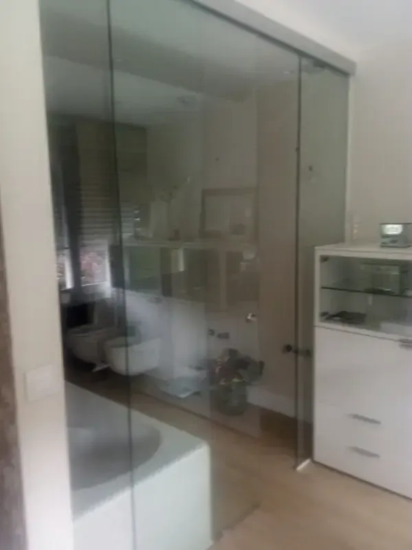 Un baño moderno con ducha acristalada, bañera blanca y mueble blanco, visible a través de una gran puerta de cristal.