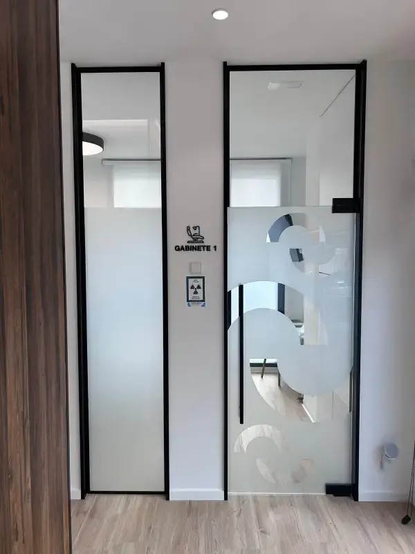 Dos modernas puertas de oficina de cristal con marcos negros en un pasillo, y un símbolo de riesgo de radiación.