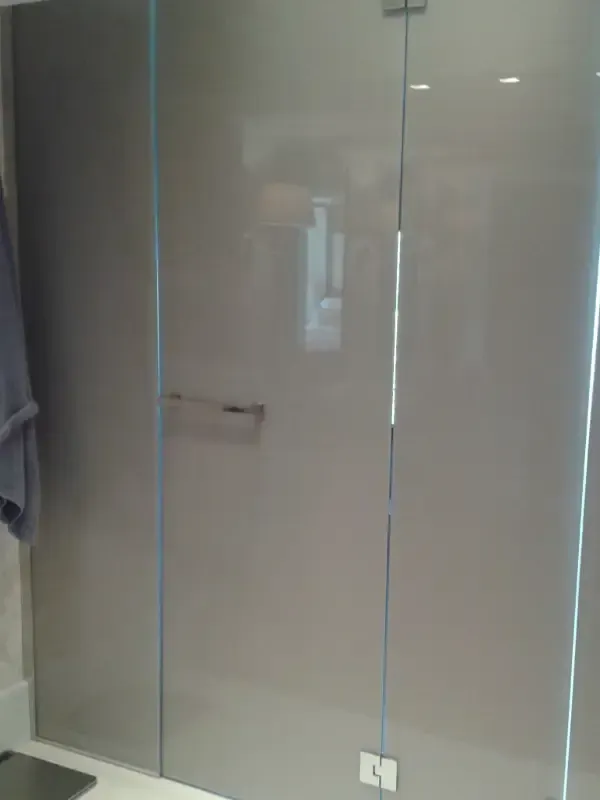 Una moderna cabina de ducha con paneles de vidrio gris, una manija de metal y un soporte de base cuadrado en un baño.