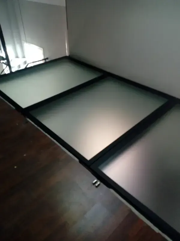 Una serie de tres paneles de vidrio esmerilado enmarcados en negro, instalados sobre un suelo de vidrio pisable.