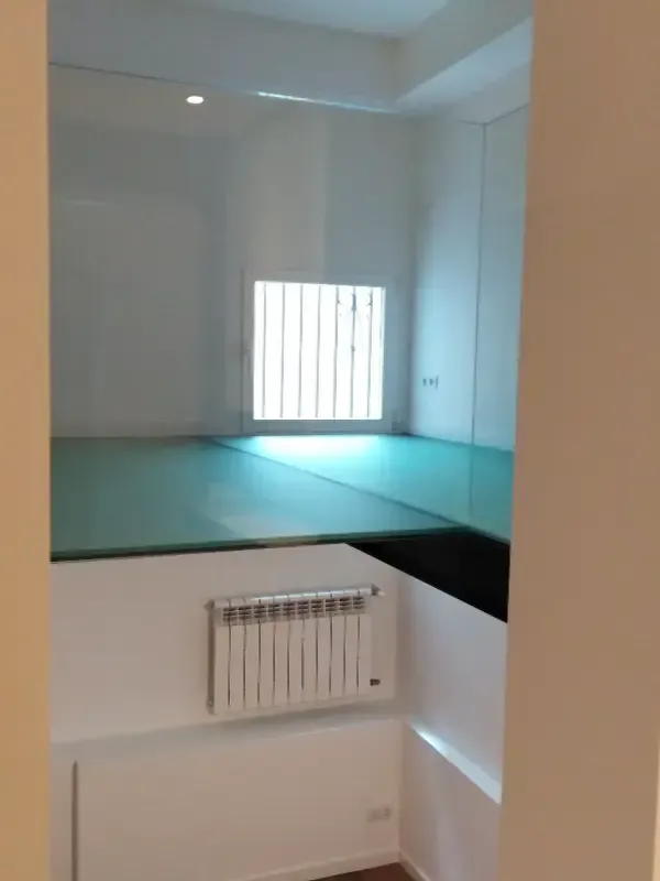 Una habitación blanca y moderna con una plataforma de cristal elevada, un radiador blanco montado en la pared