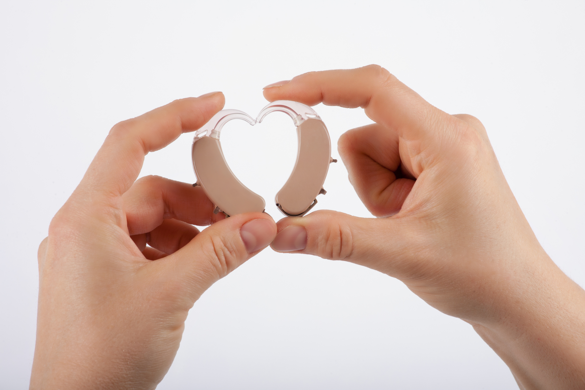 Eine Hand hält zwei Hörgeräte zusammen, welches ein Herz ergeben